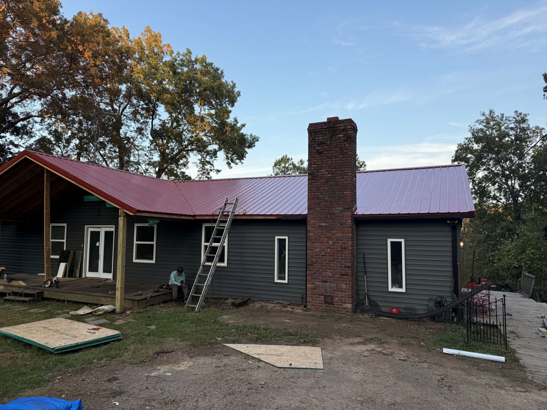 House exterior under repair with ladder, brick chimney, and purple metal roof