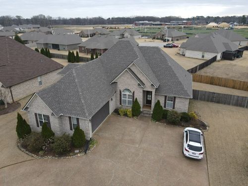 Aerial view of a large suburban house with a gravel driveway and a white car parked outside.