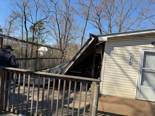 Collapsed wooden deck attached to a house, with a bent railing in a backyard.