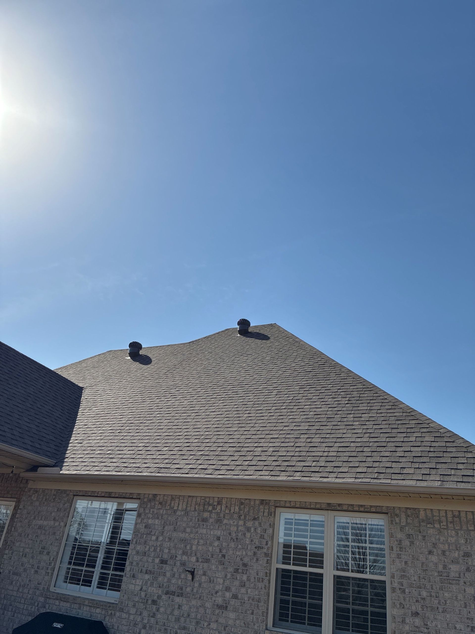 House roof with shingles under a bright blue sky and sun glare