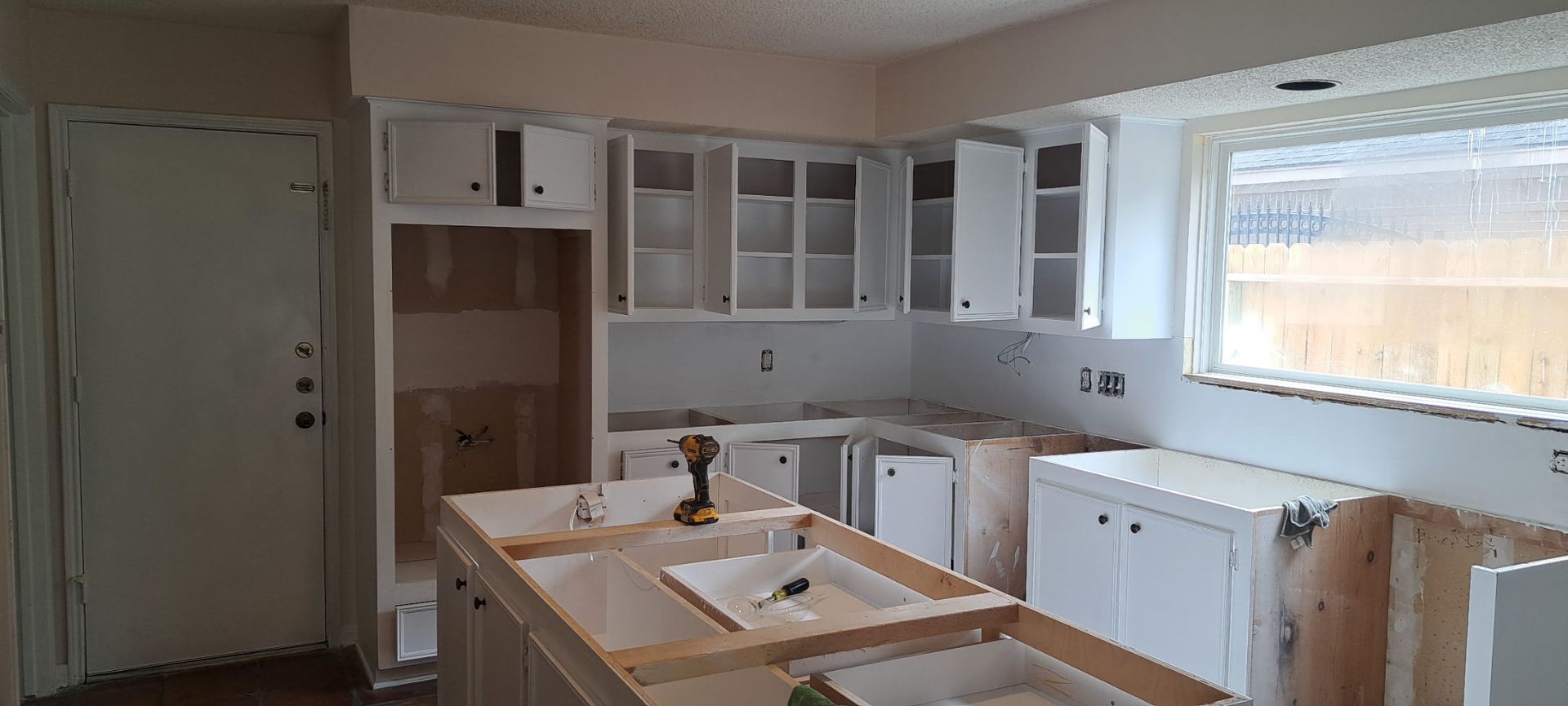 A kitchen under construction with white cabinets and a window.
