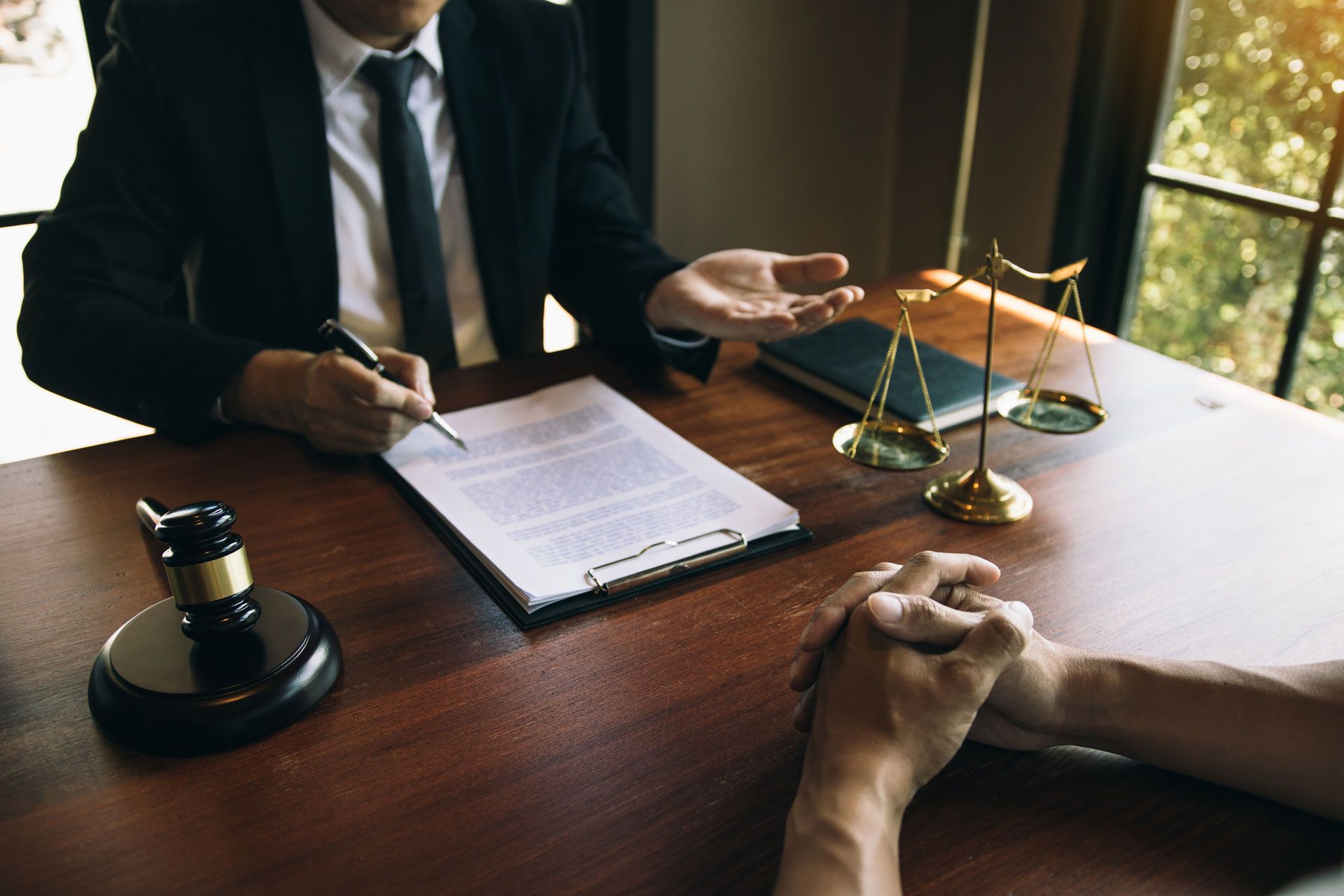 Lawyer reviewing documents with a client at a wooden table, scales of justice and gavel nearby.