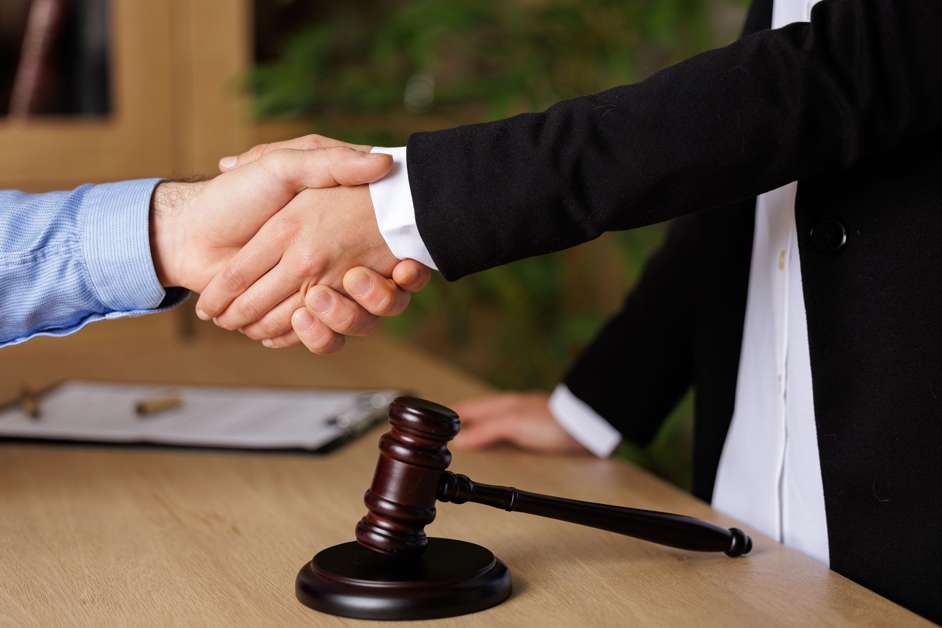 Handshake over a wooden gavel on a desk, a person in a suit, documents in the background.