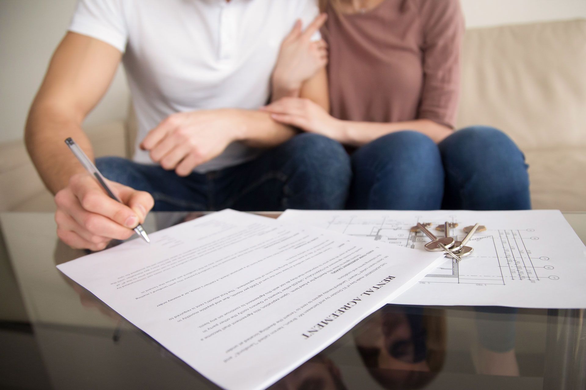 Couple signing a document on a table; keys and floor plan visible.