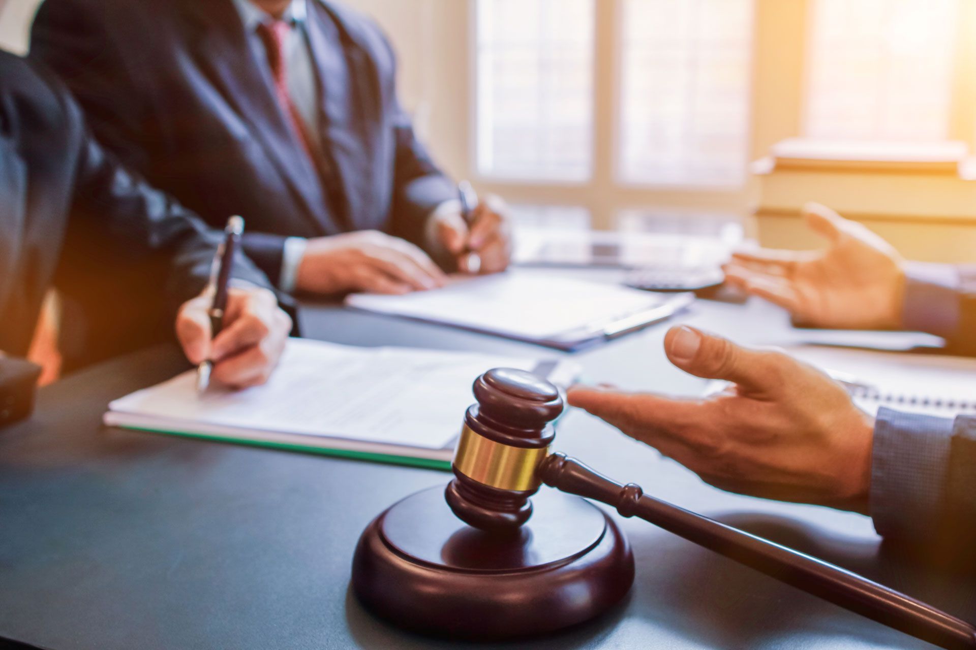 Gavel on table with people in suits, papers, and hands gesturing during a legal discussion.