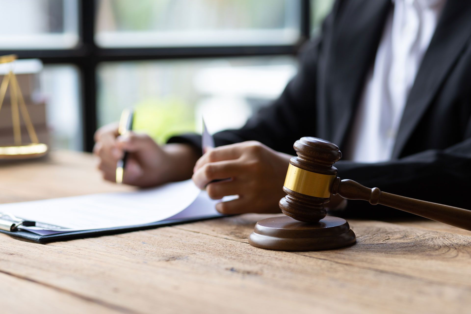 Gavel on wooden desk next to legal papers, a person in a suit writes.