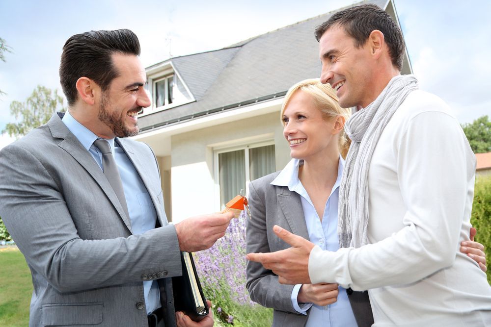 A Realtor Hands a Set of Keys to a Smiling Couple — Richardson Conveyancing In Tumbi Umbi, NSW