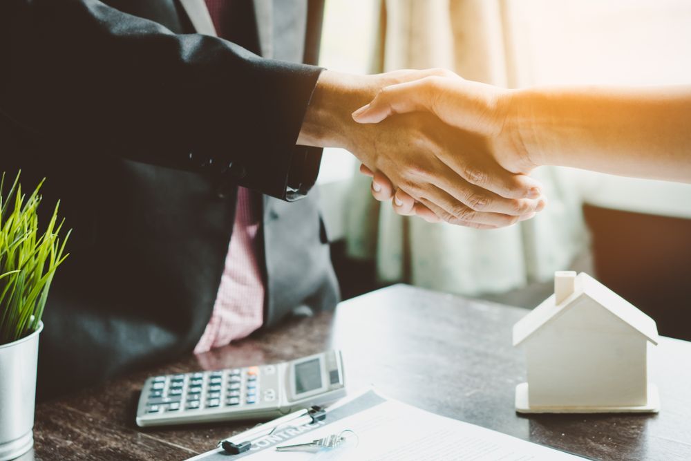 A Close-up of a Business Handshake Over a Desk With a Calculator — Richardson Conveyancing In Erina, NSW