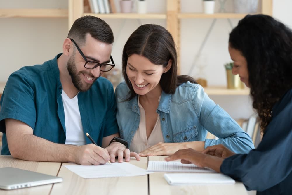 A Smiling Couple Signs a Document While Meeting With an Advisor in a Bright — Richardson Conveyancing In Tumbi Umbi, NSW