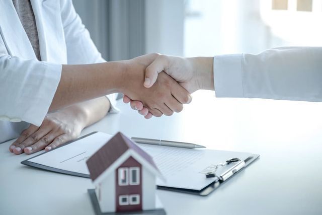 Two People Shake Hands Over a Contract Next to a Model House on a Desk — Richardson Conveyancing In Tumbi Umbi, NSW