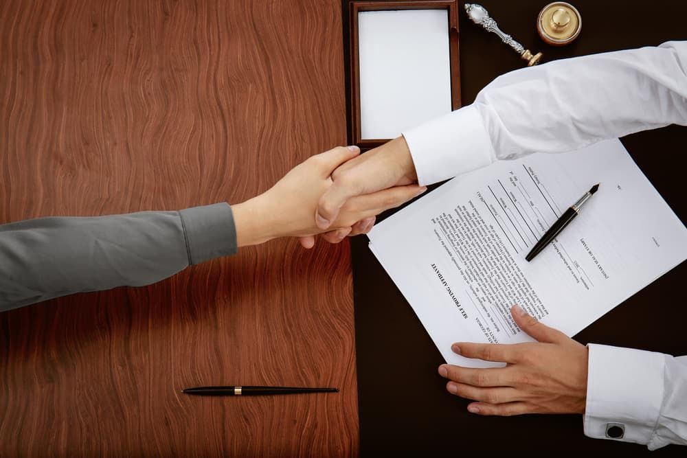Two People Shake Hands Over a Desk With a Contract and Pen — Richardson Conveyancing In Erina, NSW