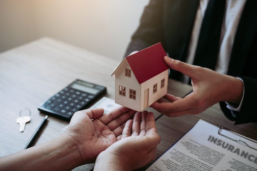 A Person in a Suit Hands a Small Model House to Another Person’s Open Hands — Richardson Conveyancing In Tumbi Umbi, NSW