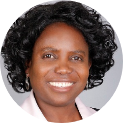 A woman is sitting at a desk with a laptop and a vase of flowers.