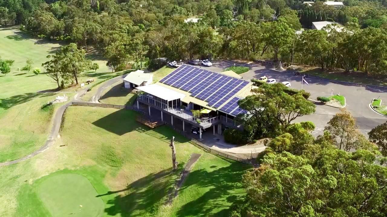 An aerial view of a building with solar panels on the roof surrounded by trees.