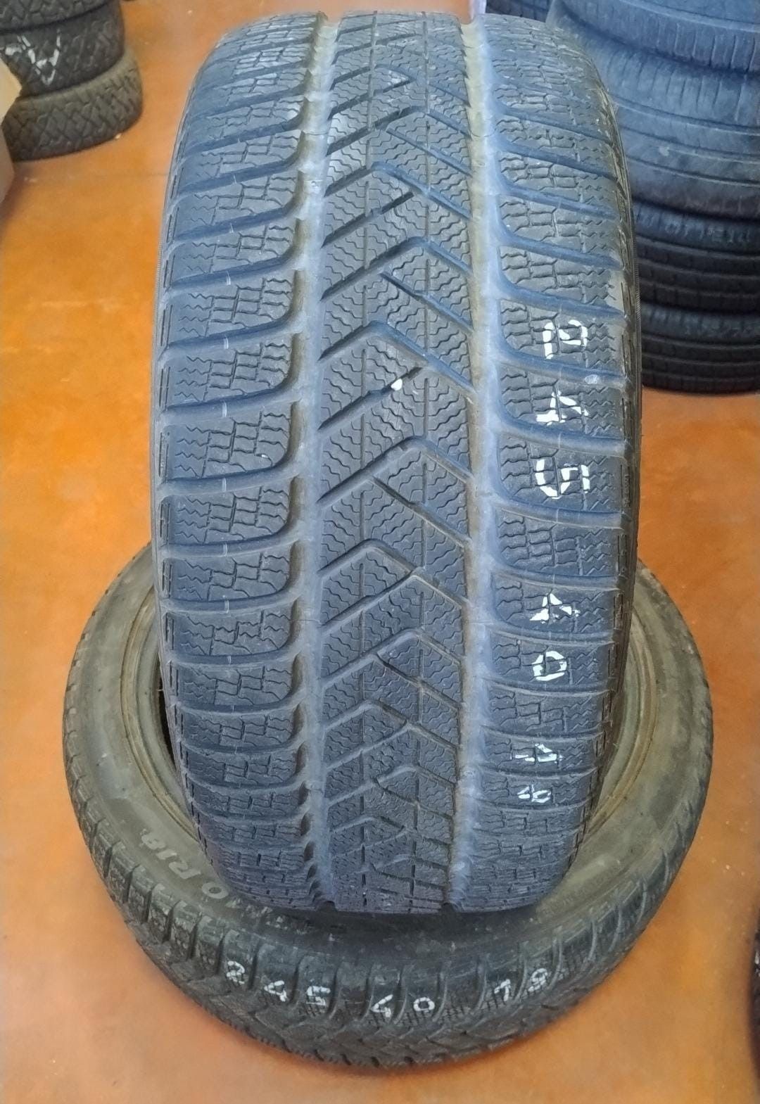 Uno pneumatico nuovo sopra uno usato, entrambi neri con battistrada scolpito, su un pavimento arancione.