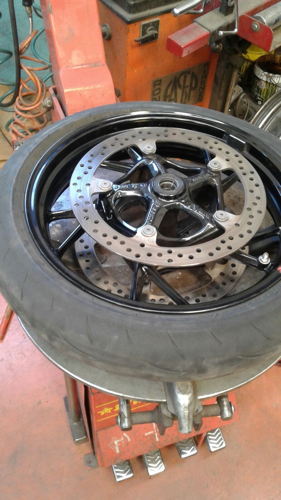 Ruota di motocicletta con pneumatico montato su una macchina smontagomme. Ruota nera, dischi freno argentati.