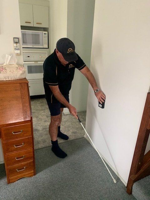A Man Is Measuring A Wall With A Tape Measure — Suncoast Termite & Pest In Caloundra, QLD