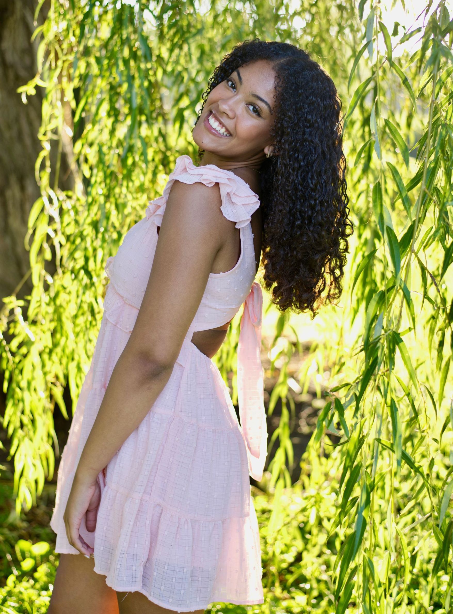 A woman in a white top and brown shorts is standing on a sidewalk with her hands on her hips.