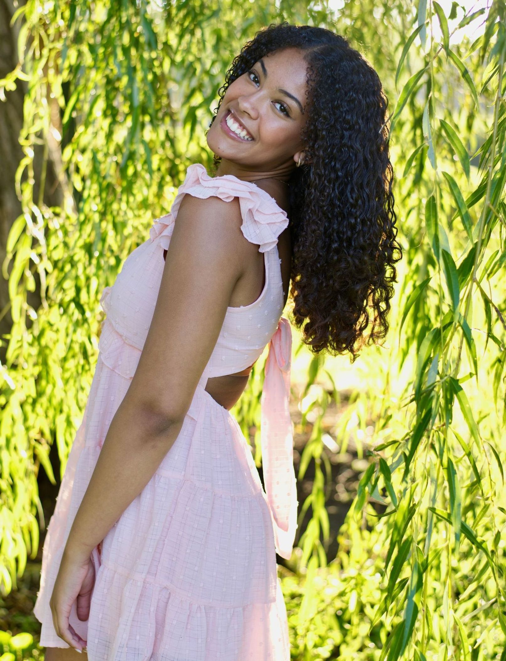 A woman in a white top and brown shorts is standing on a sidewalk with her hands on her hips.