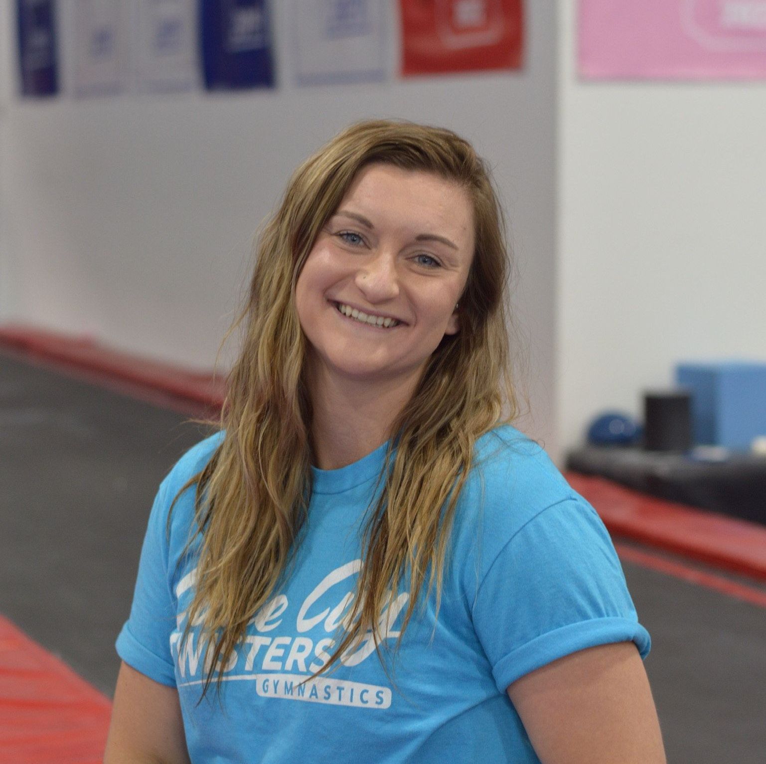 A woman in a blue shirt is smiling in a gym.