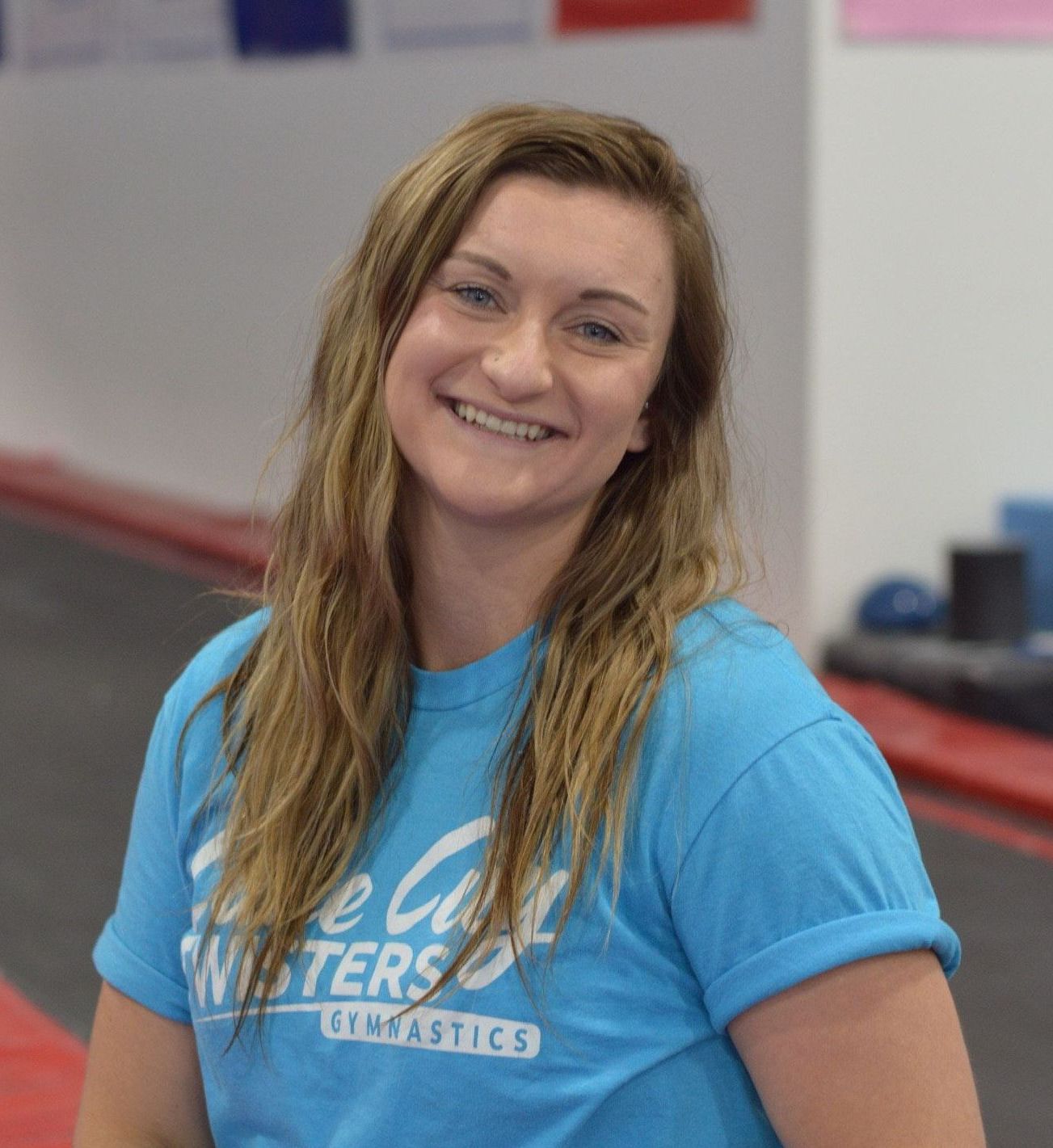 A woman in a blue shirt is smiling in a gym.