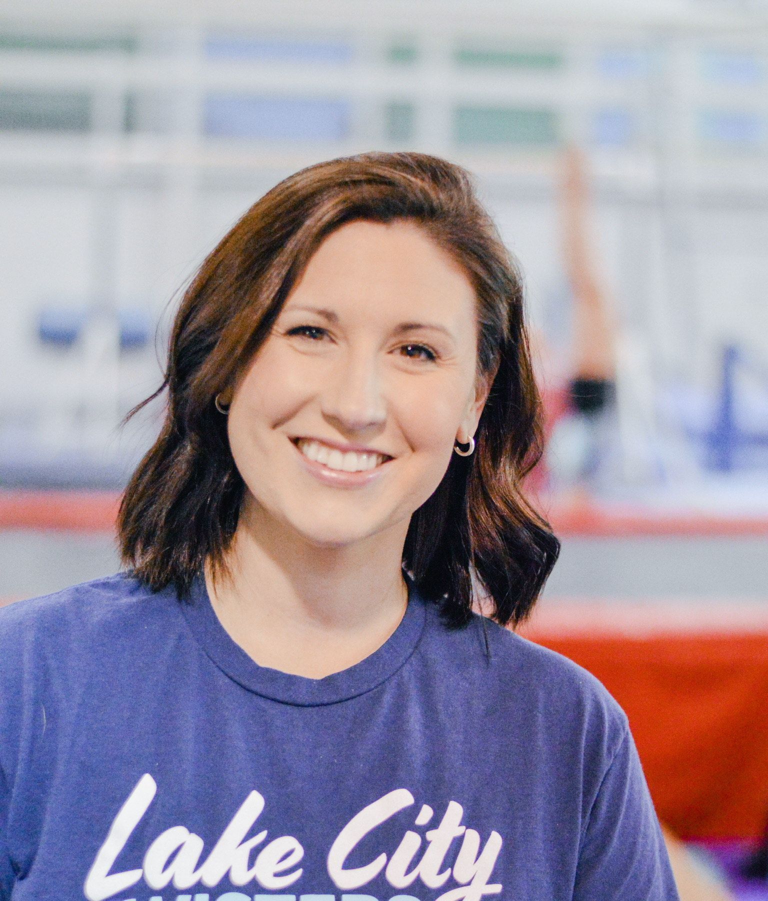 A woman wearing a blue lake city shirt is smiling for the camera.