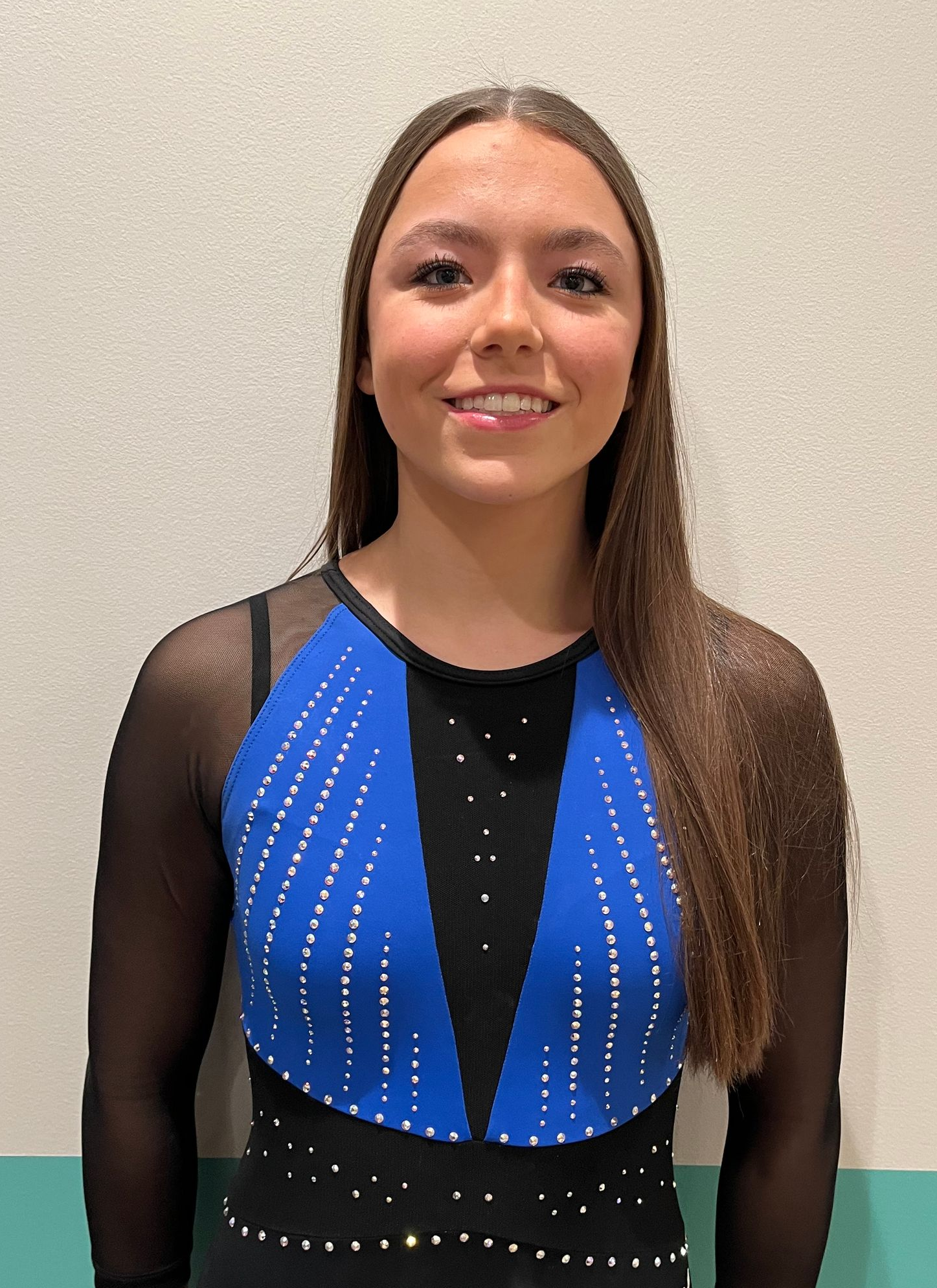A woman in a white top and brown shorts is standing on a sidewalk with her hands on her hips.
