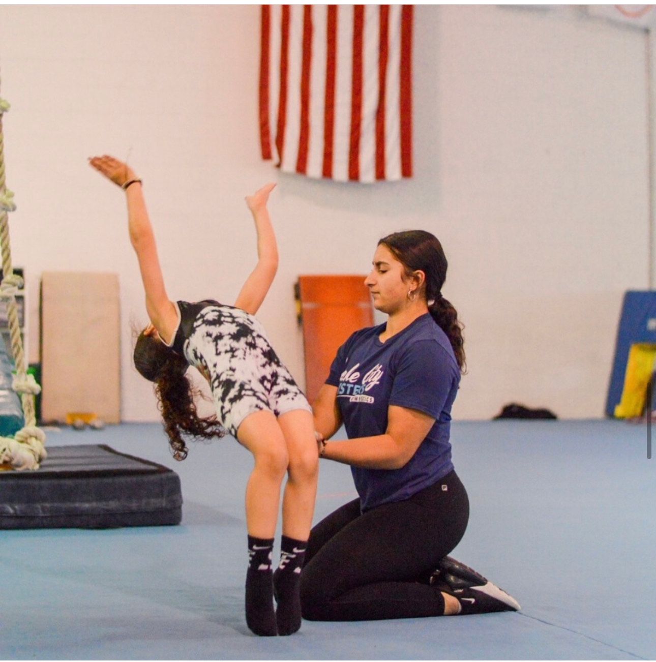 A woman kneeling down helping a young girl do a trick