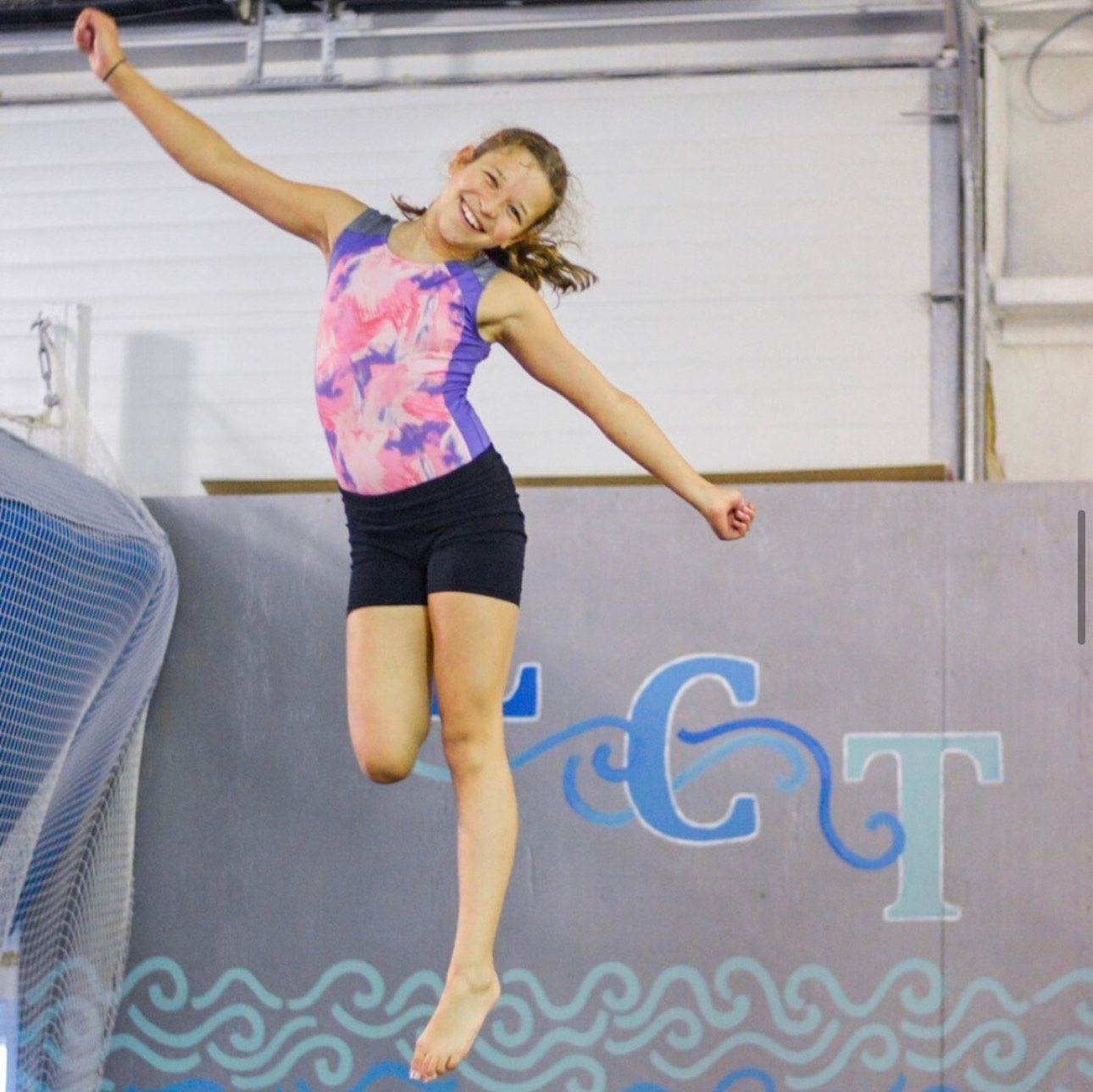 A young girl is jumping in the air in front of a wall that says gt