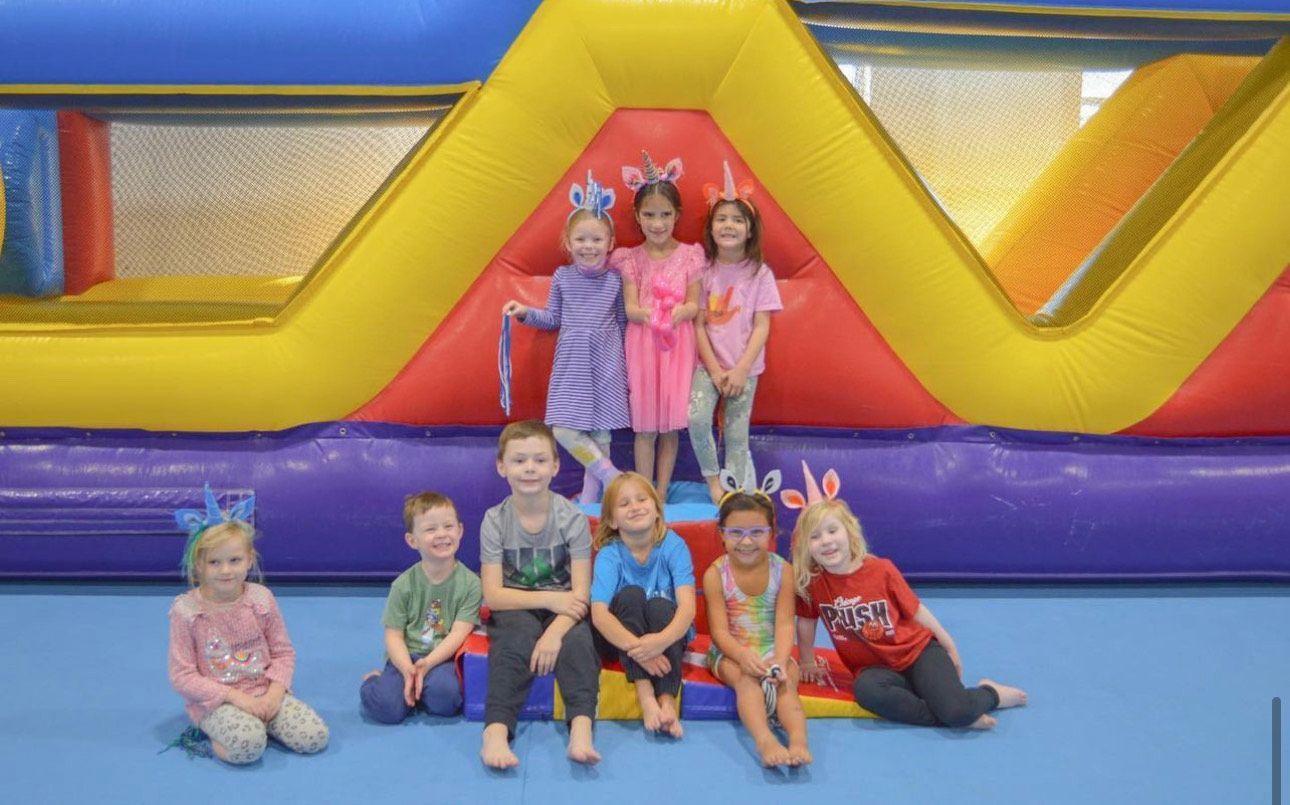 A group of children are posing for a picture in front of a bouncy house.