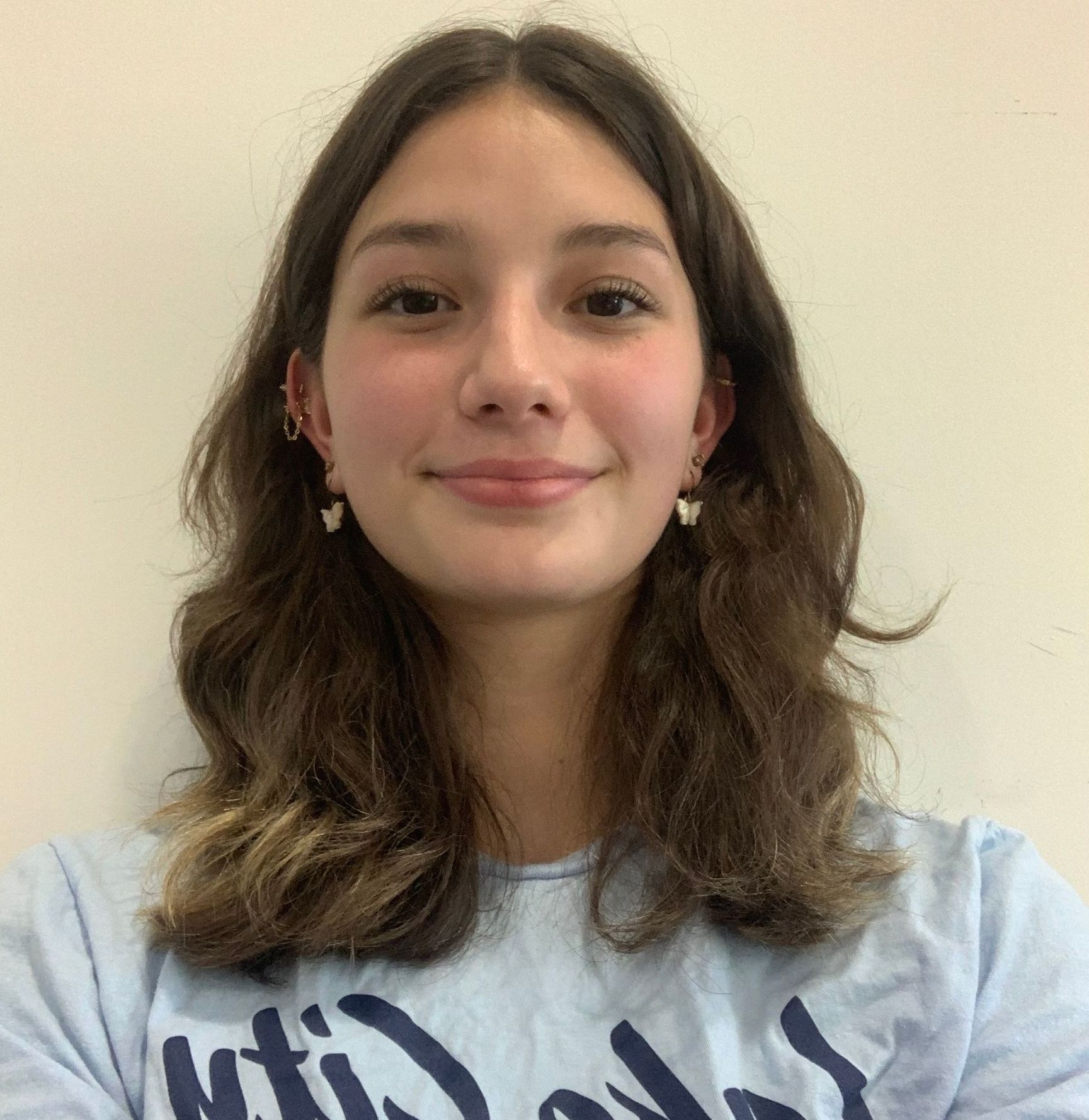 A young woman wearing a blue shirt with the word wild on it is smiling for the camera.