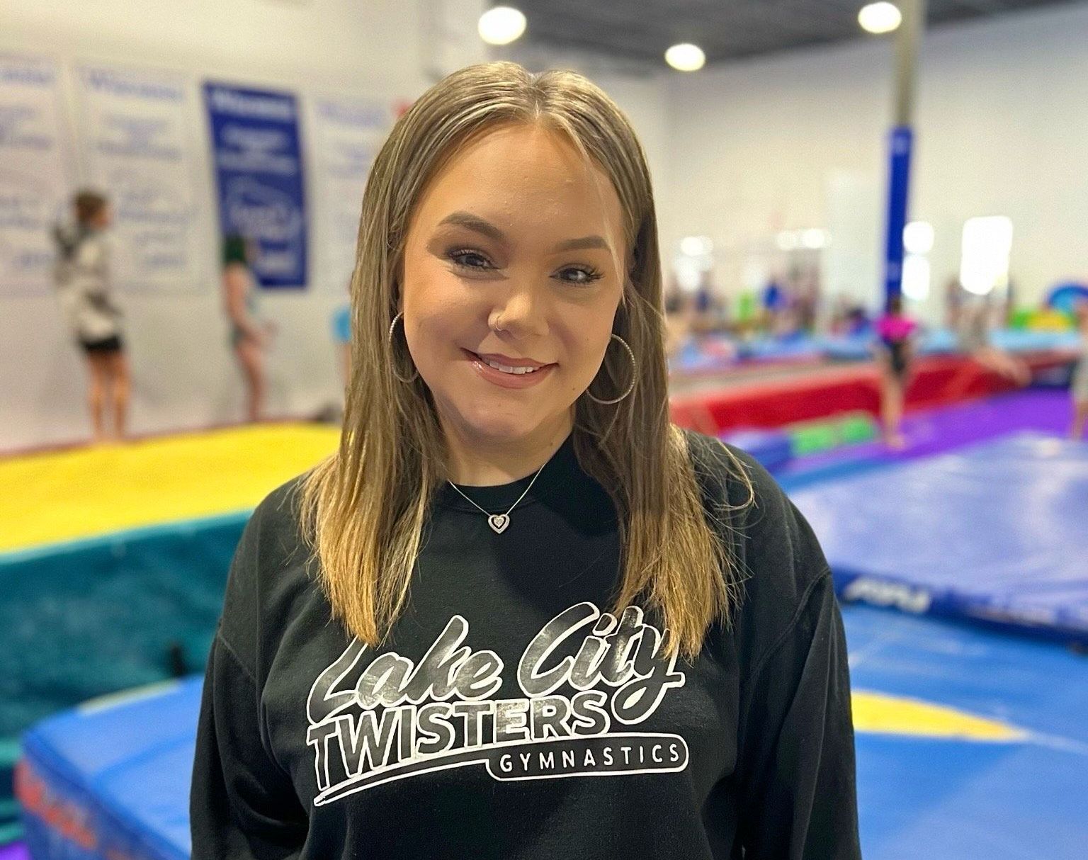 A young woman wearing a black sweatshirt is standing in a gym.