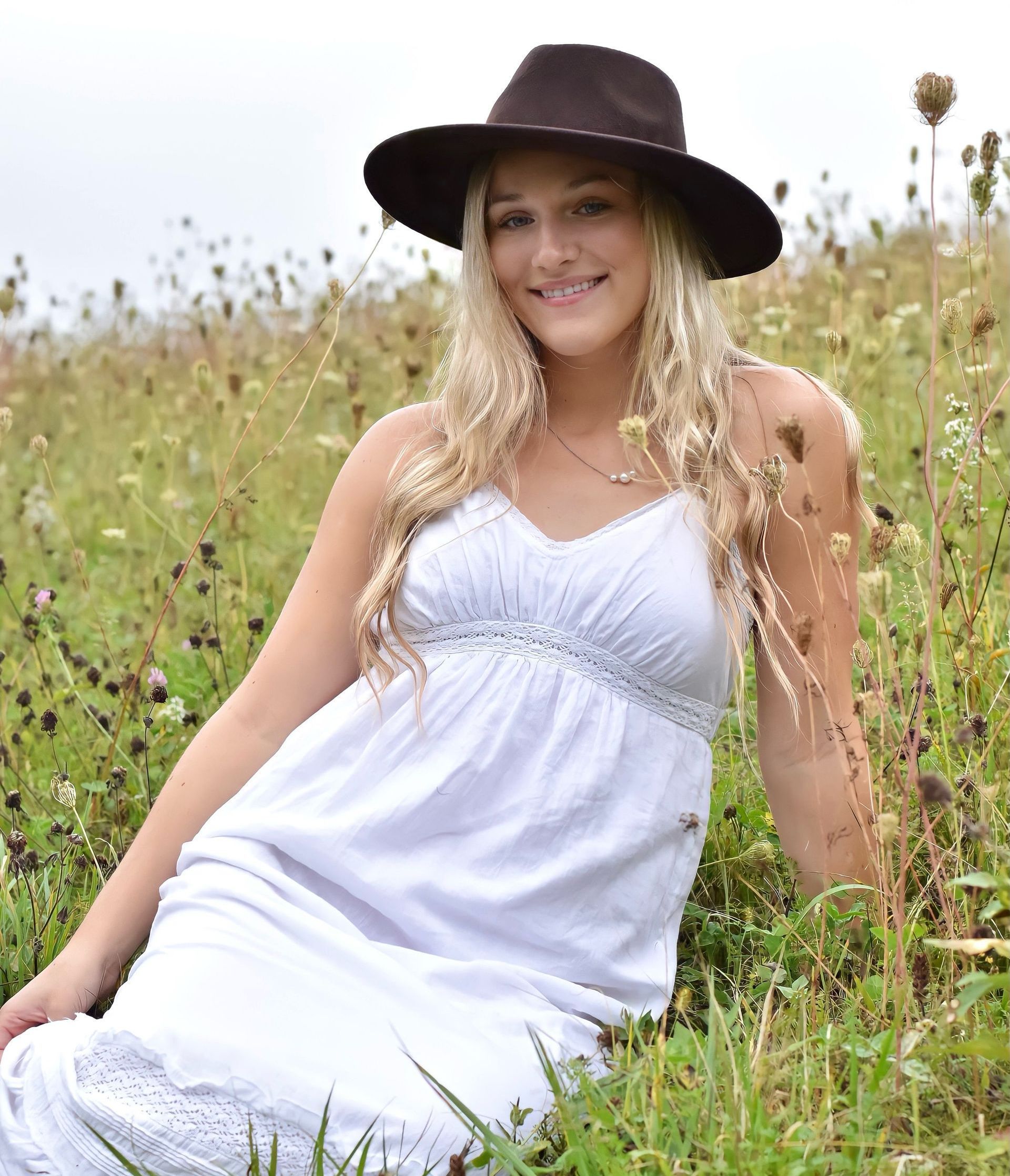 A young woman is sitting on a bench in front of a bush and smiling.