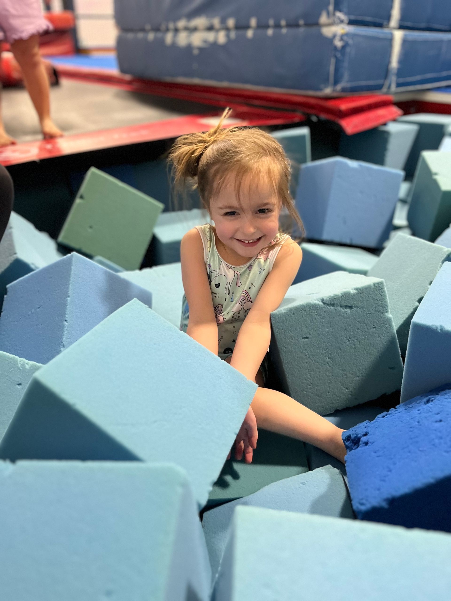 A little girl is sitting in a pile of foam blocks.