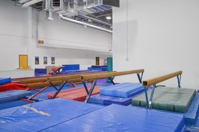 A row of balance beam in a gym with blue mats.