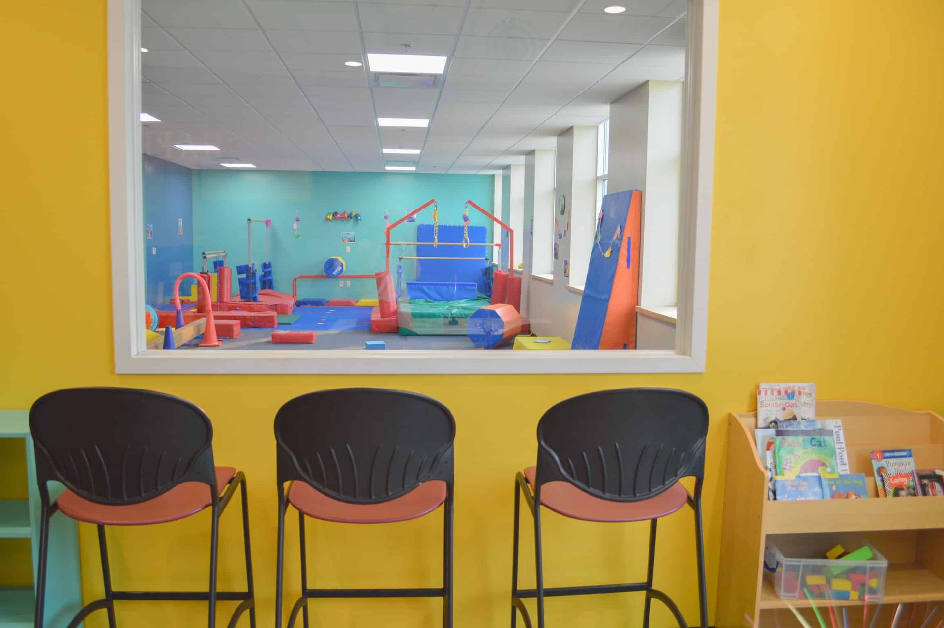 A view of a gym through a window with three chairs in front of it.