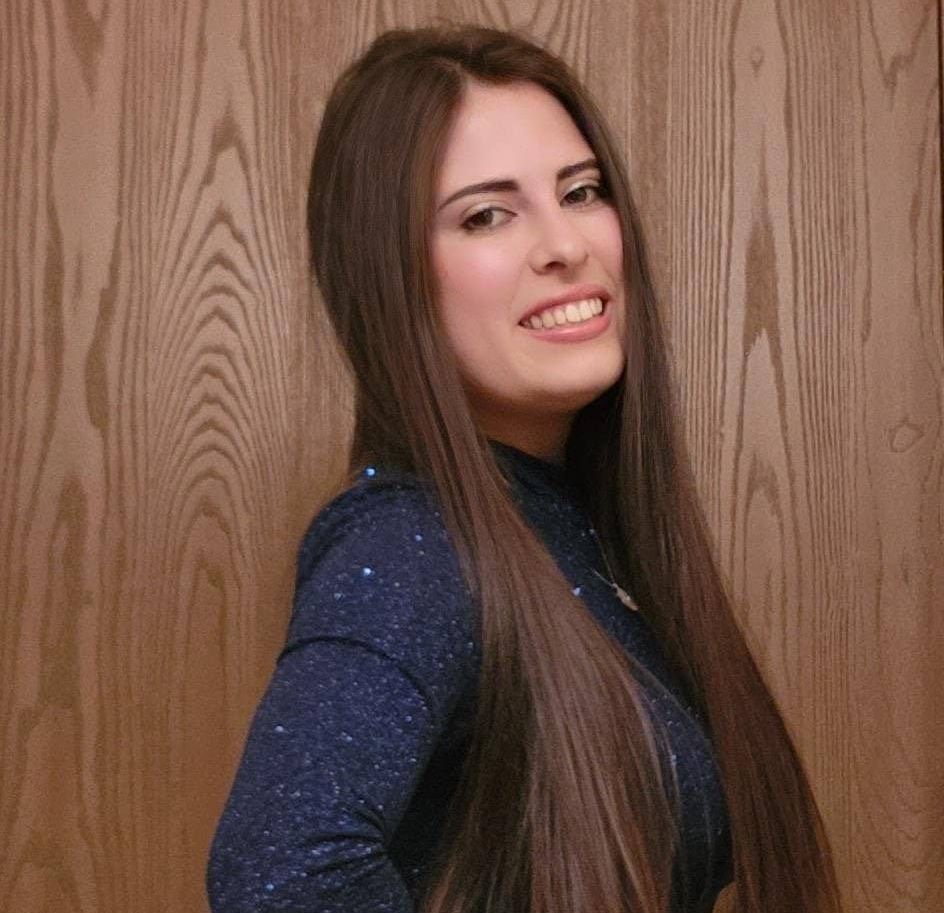 A woman with long hair is smiling in front of a wooden wall.