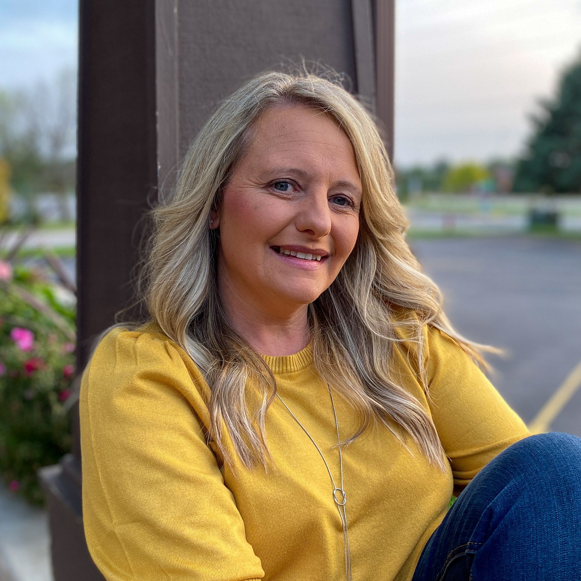 A woman in a yellow sweater is sitting next to a pole and smiling.