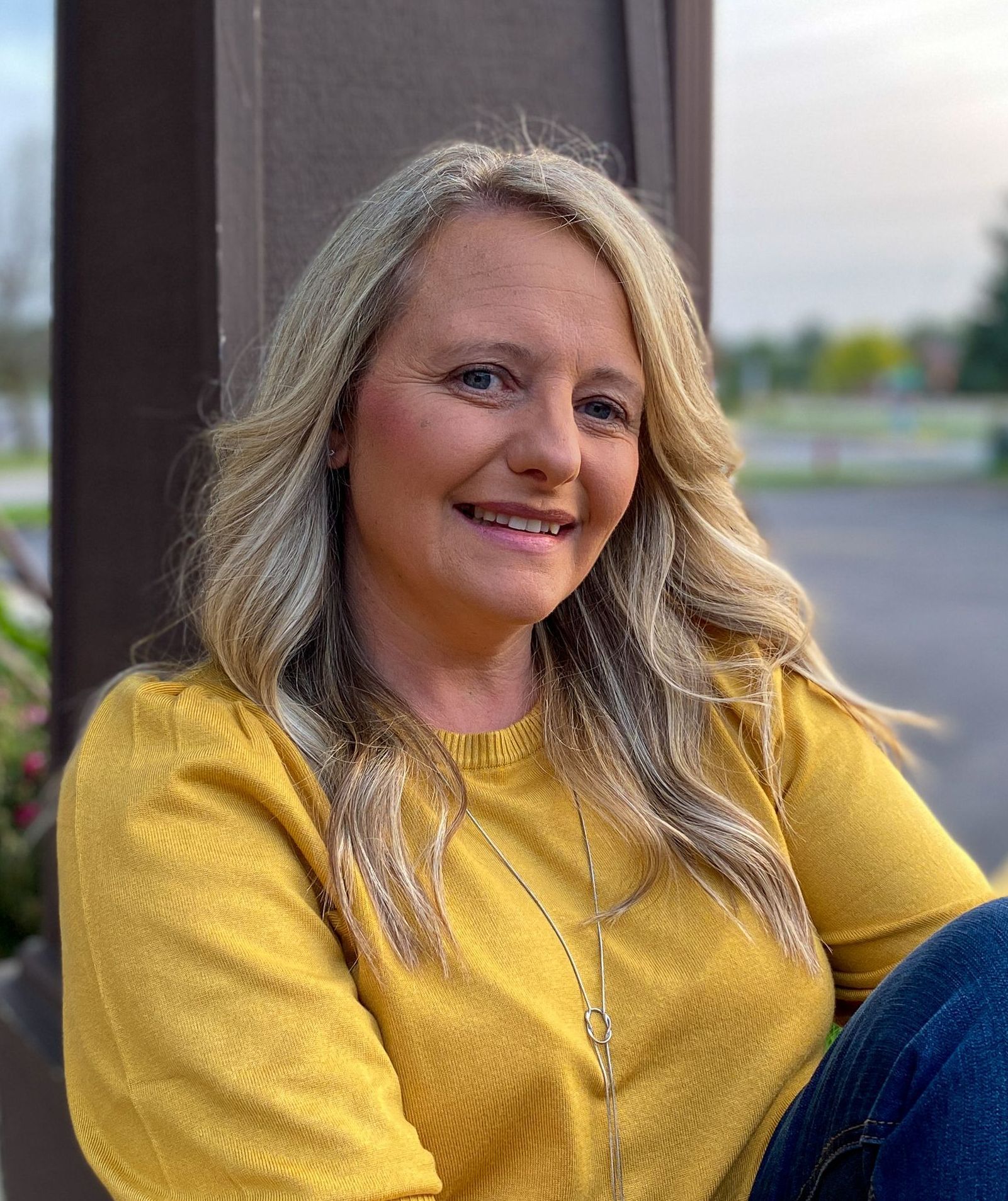 A woman in a yellow sweater is sitting next to a pole and smiling.