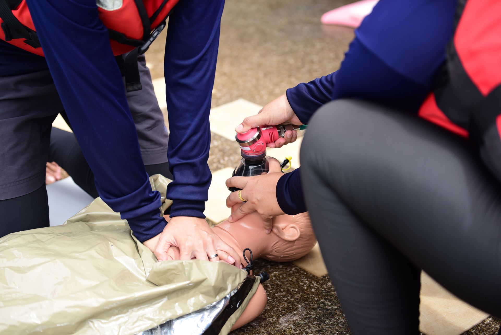 Two people practice CPR on a dummy, one giving chest compressions, the other with a resuscitator.