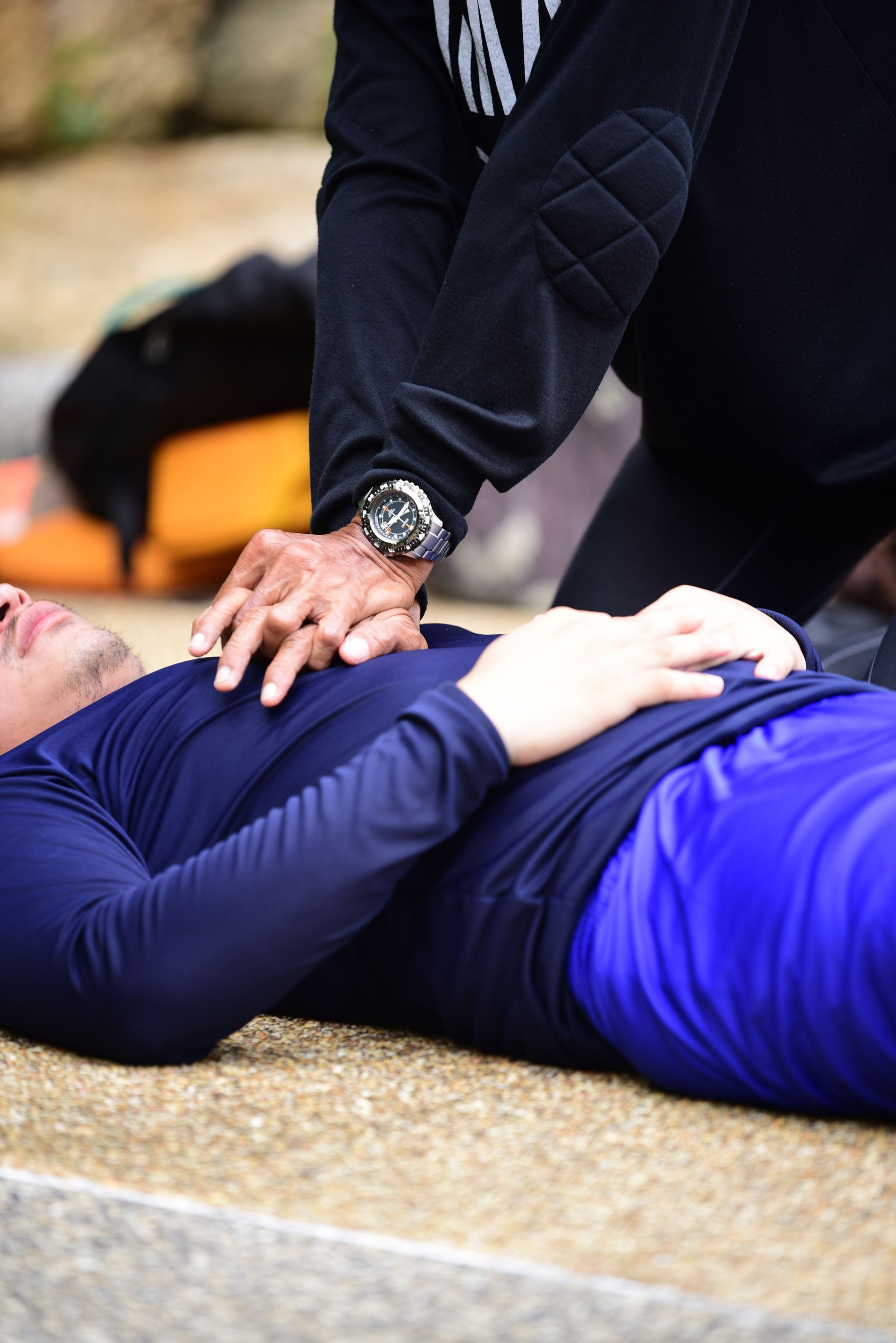 Person receiving CPR on the ground. Another person kneels, hands on the first person's chest.