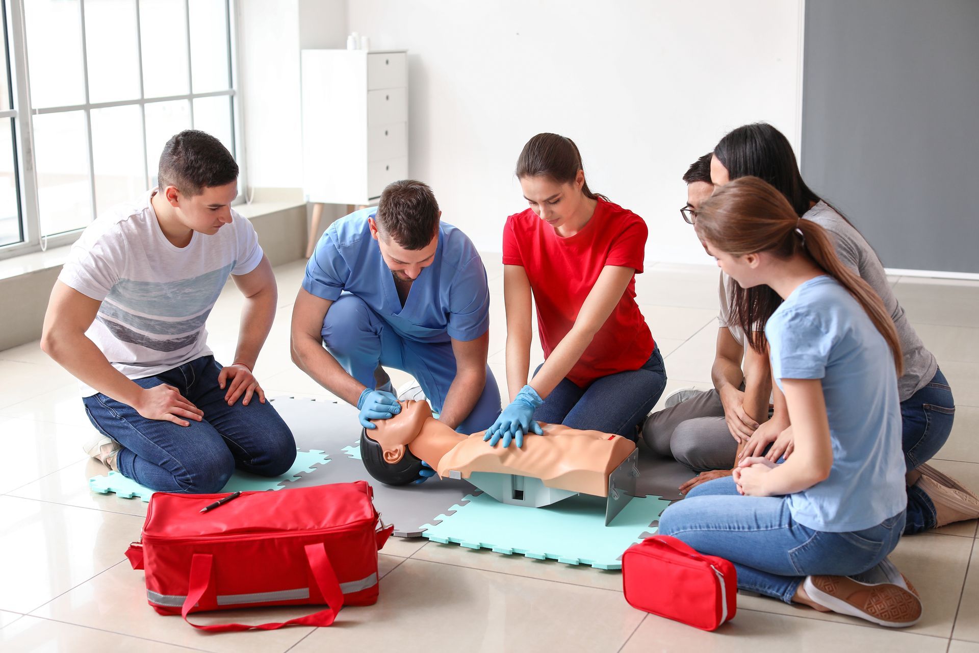 Group practicing CPR on a training dummy, led by an instructor, in a classroom.