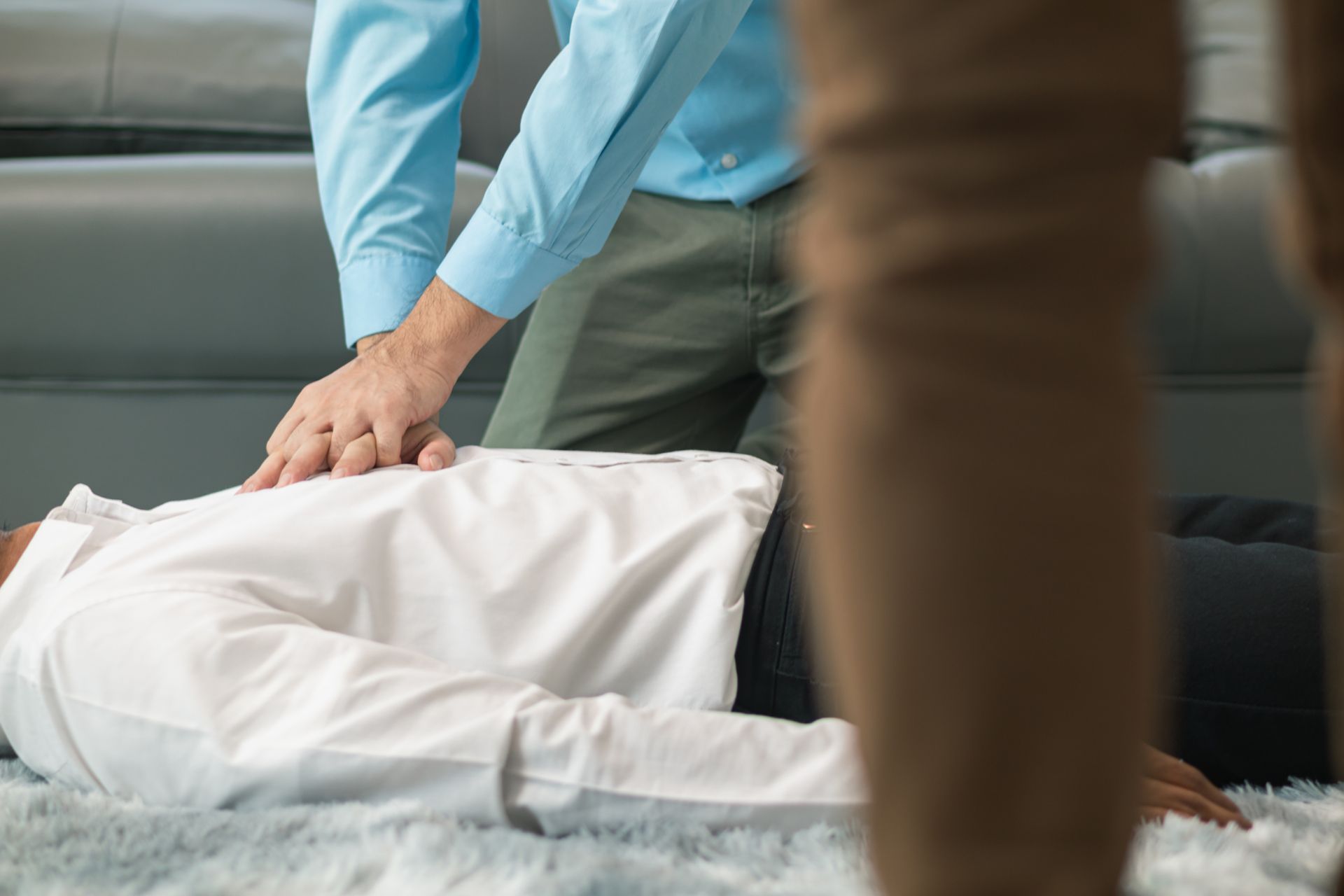 Person performing CPR on someone lying on the floor; another person stands nearby.