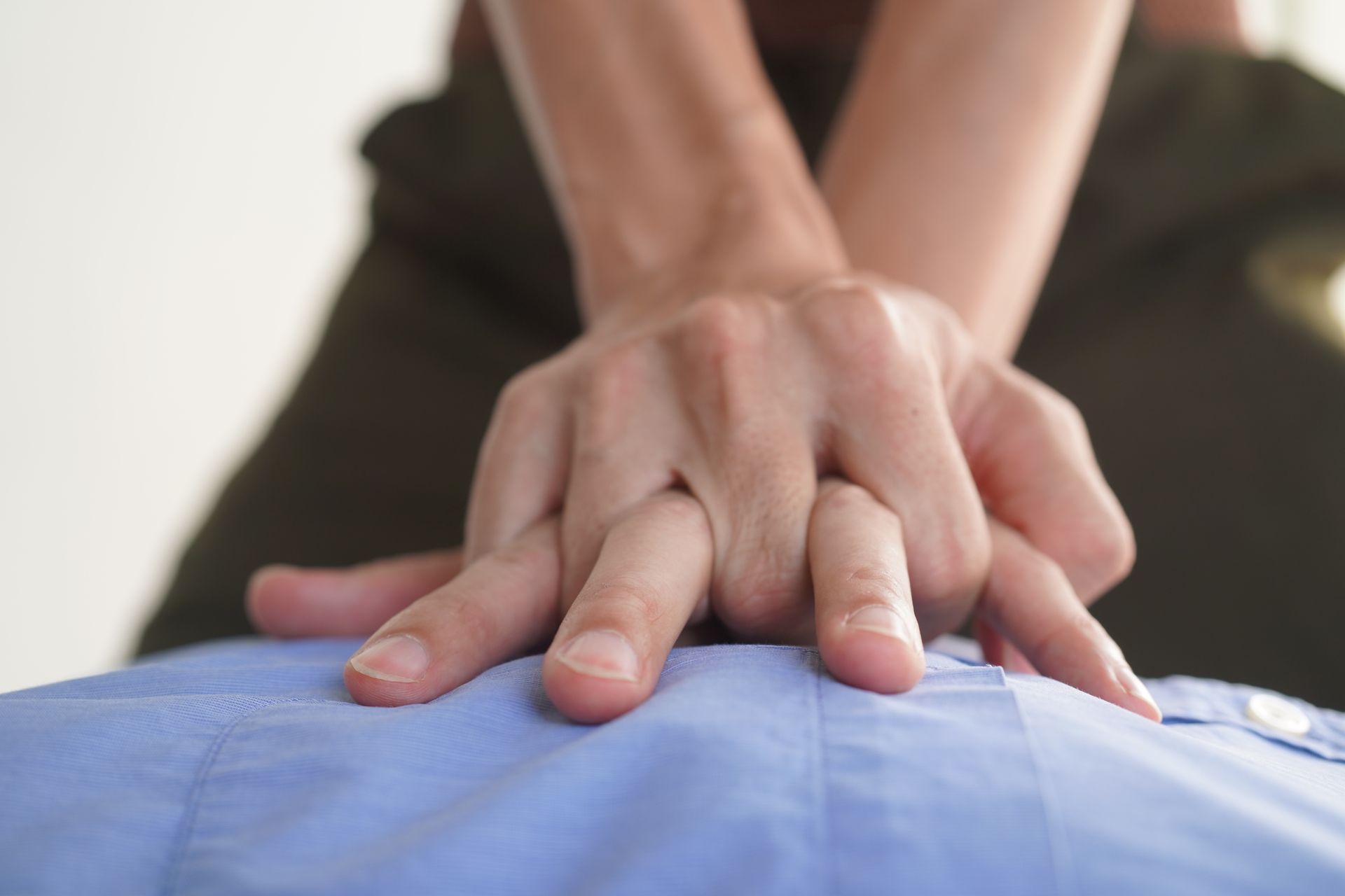 Hands performing CPR on a person wearing a blue shirt.