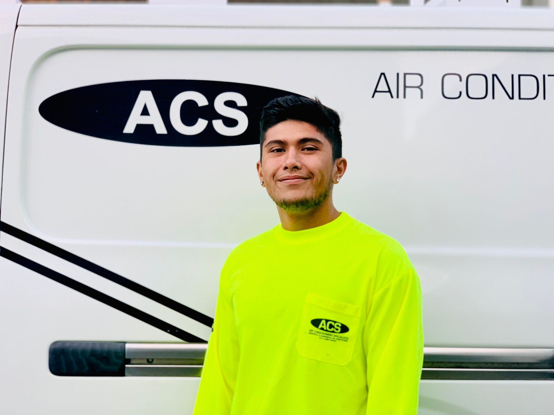 A person wearing a yellow shirt standing in front of a white work van labeled with