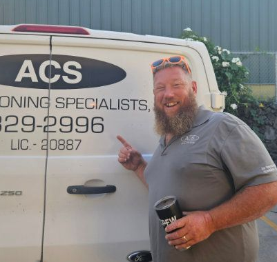 A smiling person with a beard stands by a work van labeled