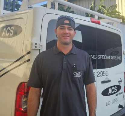 A technician in a black ACS company shirt stands in front of a white work van with ACS branding.