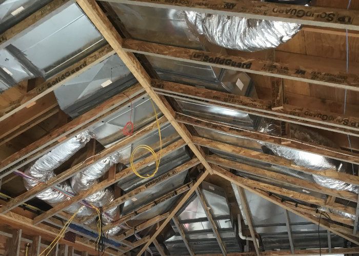 Exposed wooden roof trusses in an unfinished attic with metallic insulation panels and flexible silver air ducts.