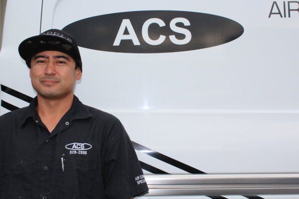 A technician in a black uniform standing in front of a white van with an ACS logo.