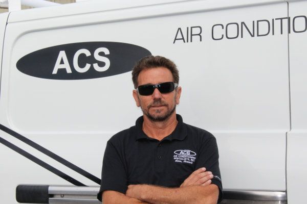 A man in a black polo shirt with arms crossed, standing in front of a white service van labeled